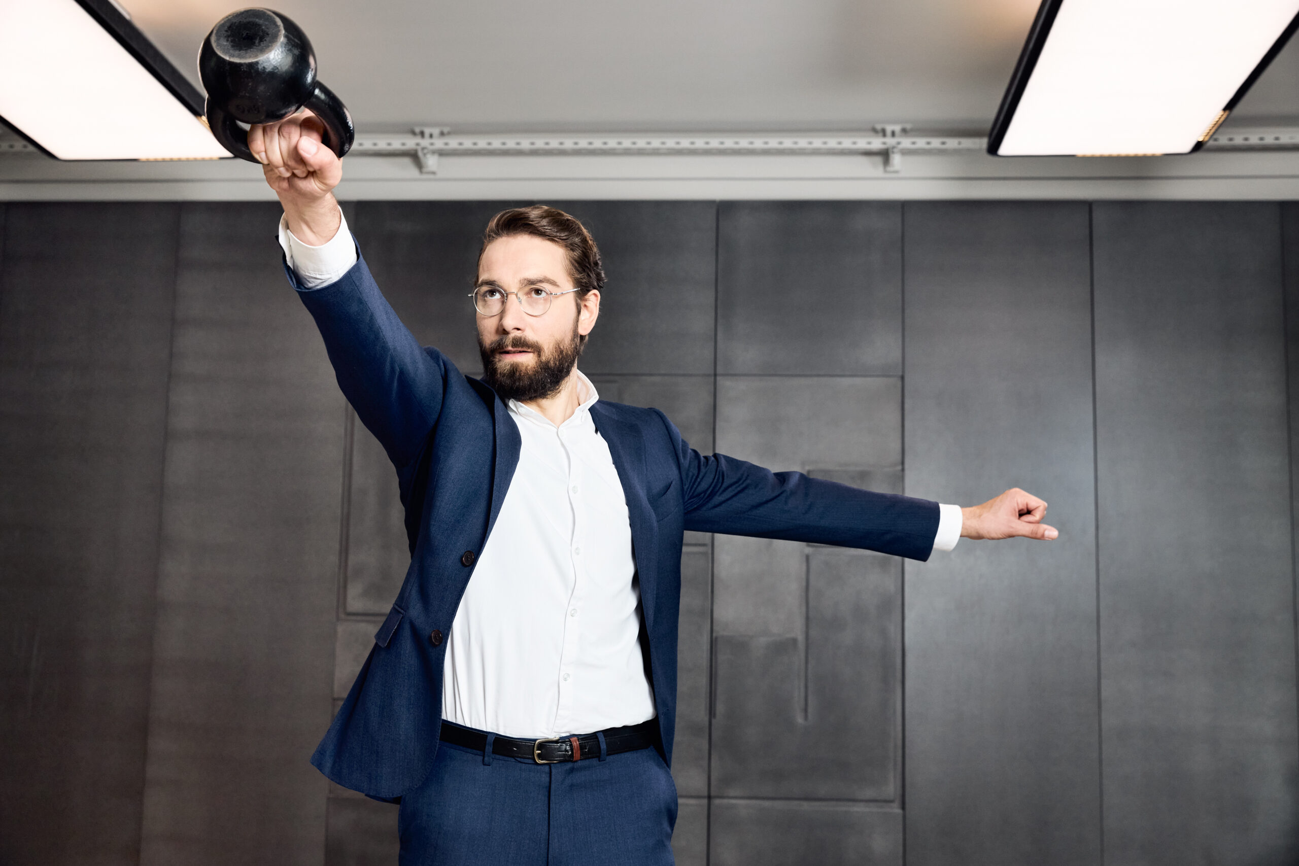 Der Projektleiter, Chris Schiebel, steht im Fitness-Studio und schwingt aktiv in Businesskleidung eine Kettlebell.