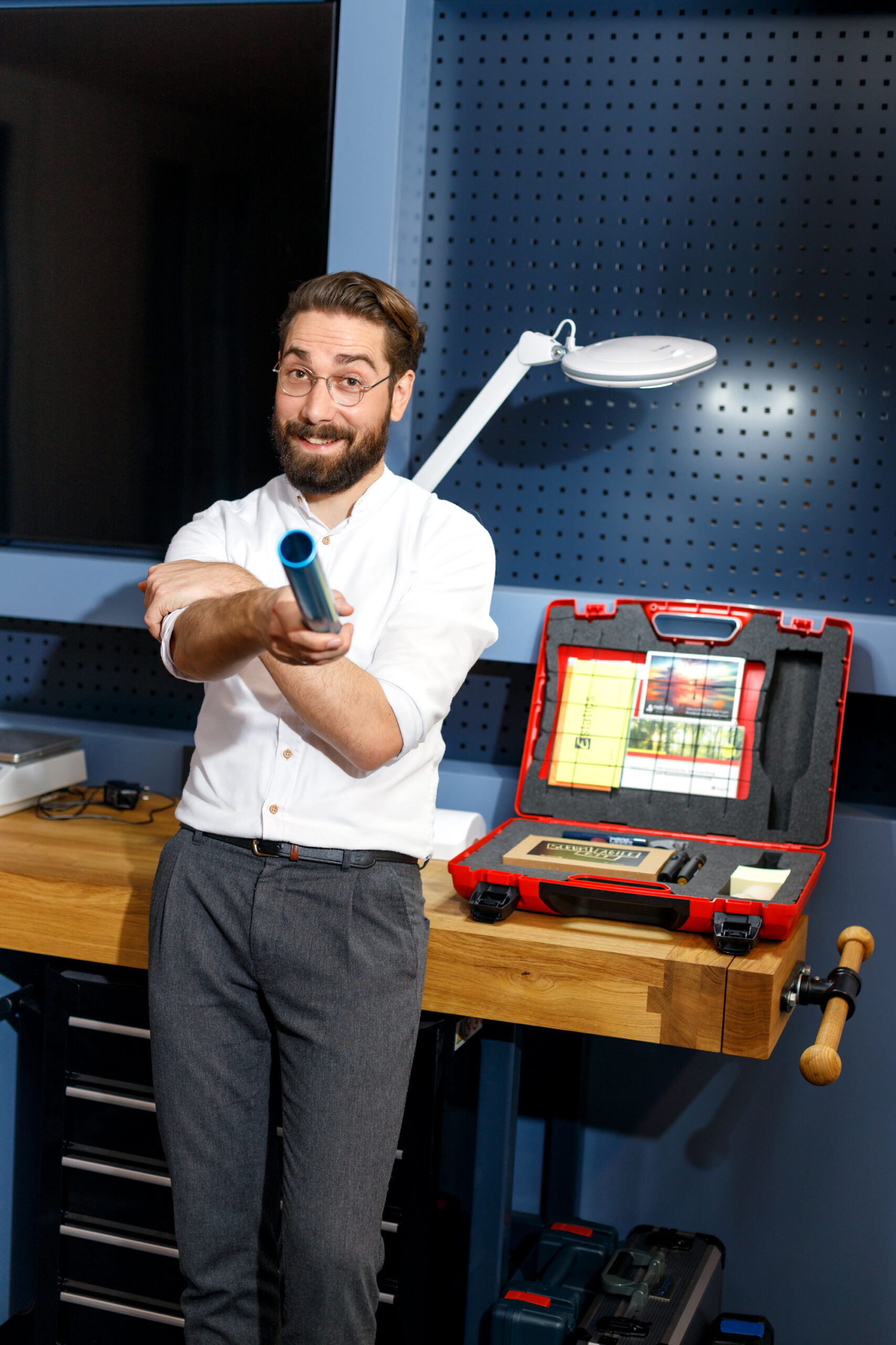 Chris Schiebel, der Projekt Botschafter, lehnt an einem Schreibtisch und reicht einen Staffestab in Richtung Camera. Er schaut auffordernd.